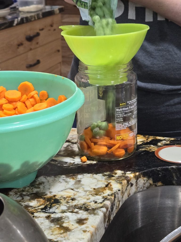 Adding peas to a jar of carrots through a funnel