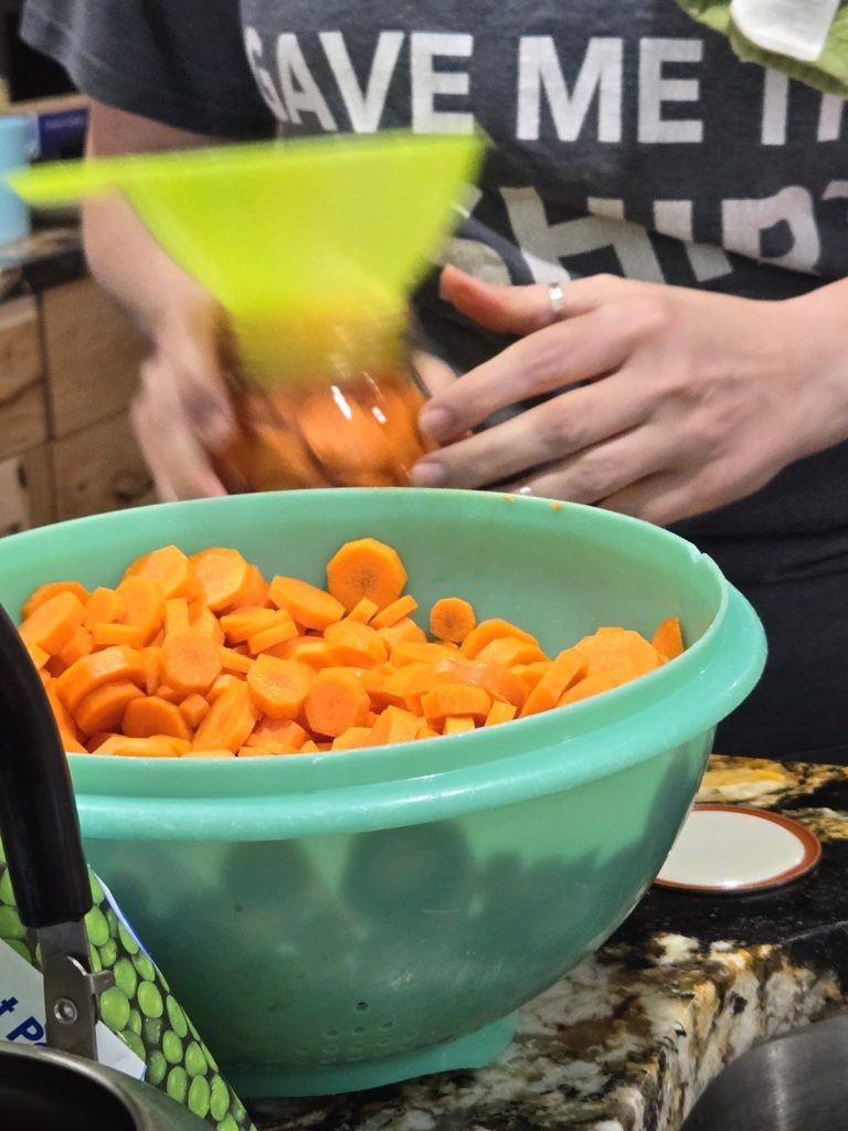 Filling a jar with sliced carrots through a green funnel